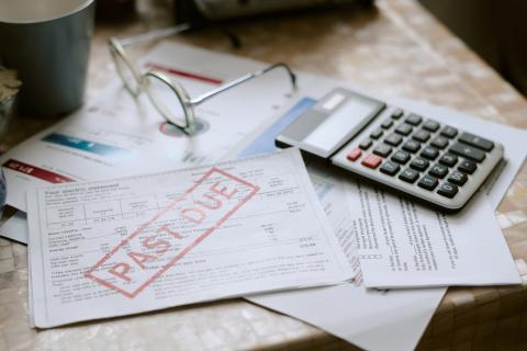A pile of bills on a desk, with the top billing stamped "past due" next to a calculator.